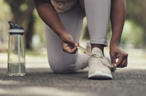 A woman tying her shoelace and preparing for an outdoor physical activity with a bottle of water by her leg