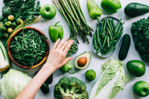 Woman hands taking green peas from table with fresh vegetables, healthy nutrition concept.